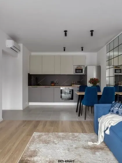 This open-plan layout showcases a bold blue sofa that adds a pop of color, connecting the living area with the sleek, modern kitchen and dining space.