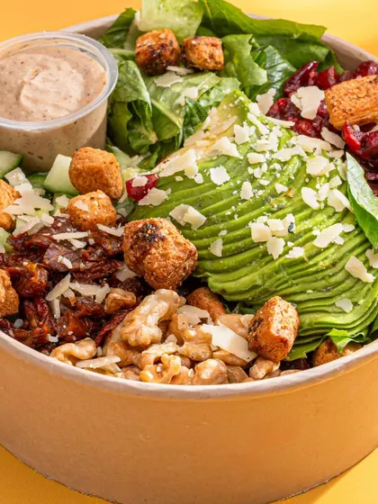 An avocado salad from Herbivore Farms. The focus is on the beautifully fanned avocado and the mix of healthy ingredients, appealing to health-conscious customers.