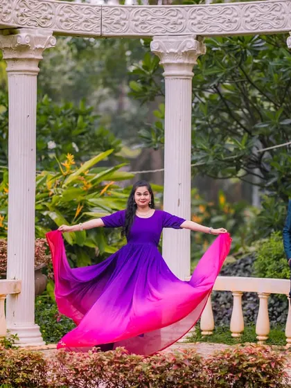 A playful and elegant pose among the white pillars. The bride-to-be shows off her beautiful purple and pink ombre gown while her partner looks on, creating a lovely, balanced composition.