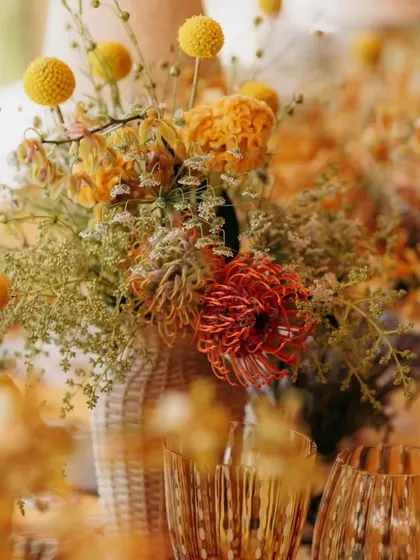 A rustic and wild floral arrangement in a woven vase, featuring unique flowers like craspedia and pincushion protea. This adds texture and a pop of color to the tablescape.