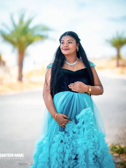A full-length view of the mother-to-be, showcasing the elegant maternity gown against a simple, bright background. This highlights the outfit and the beautiful baby bump.