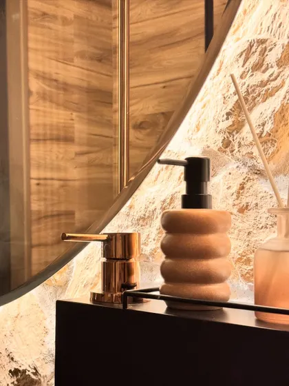 A close-up detail of the powder room. Every element is chosen with care, from the warm metallic finish of the faucet to the organic shape of the soap dispenser, all contributing to the overall feeling of a bespoke, earthy space.