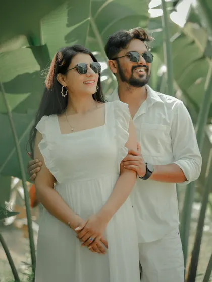 A fun and carefree moment captured against a backdrop of lush tropical leaves. The couple, dressed in matching white, shares a laugh, showcasing the relaxed and joyful side of their relationship.