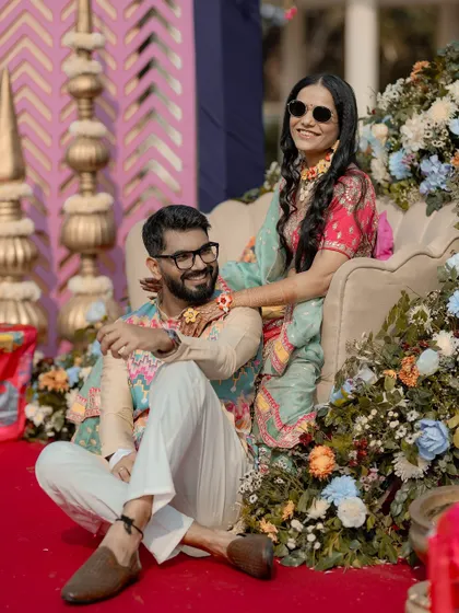 A stylish portrait of the couple at their Mehendi ceremony, looking relaxed and happy amidst the colorful floral decor.