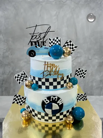 For the ultimate speed lover, I designed this two-tier BMW-themed birthday cake. It features a blue and white ombre design, checkered racing flags, and the iconic BMW logo, making it a perfect centerpiece for a car-themed party.