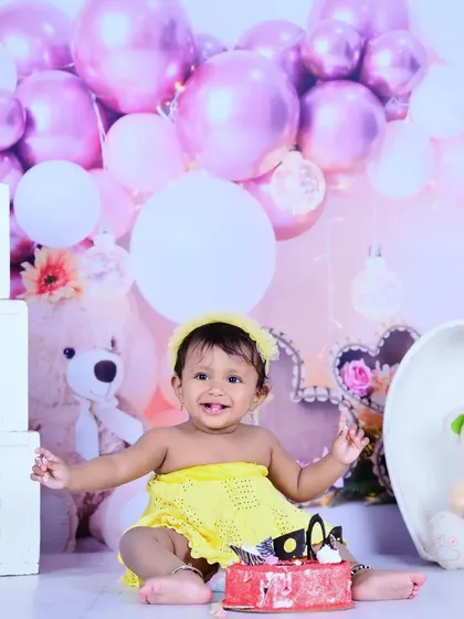 A first birthday cake smash scene with a teddy bear and balloons in the background.