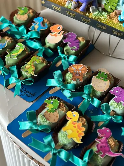 A close up of our dinosaur themed cakesicles, each decorated with a different dino sticker and a cute ribbon.