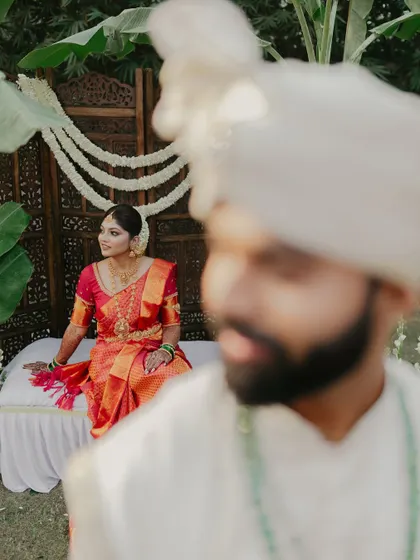 An artistic shot with the groom in the foreground, drawing focus to the beautiful bride seated behind him.