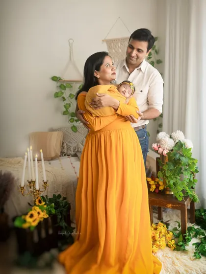 A new family stands together in a bright, sun-filled boho studio setup. The mother holds their swaddled newborn as they all look on with love, creating a warm and joyful family portrait.