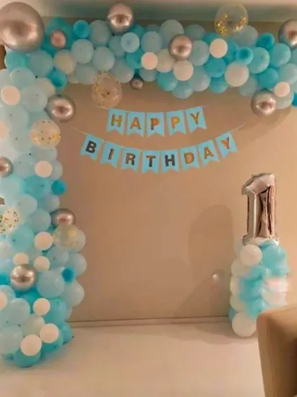 A classic blue and silver balloon arch for a first birthday. This simple yet elegant home setup includes a "Happy Birthday" banner and a number '1' foil balloon.