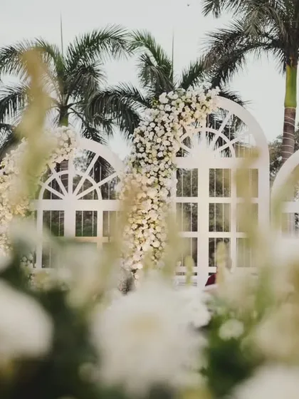 A dreamy wedding setup with white floral arches against a backdrop of palm trees, creating a beautiful, breezy, and elegant atmosphere.