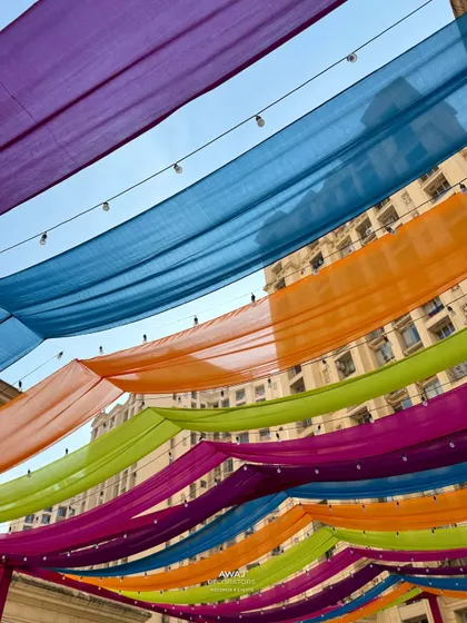 A vibrant canopy of colorful drapes in shades of purple, blue, orange, and pink, creating a festive ceiling for a Mehendi party.