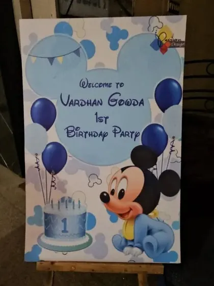 A custom welcome board for a first birthday party. This one features a baby Mickey Mouse theme with blue balloons and a cake illustration to greet the guests.