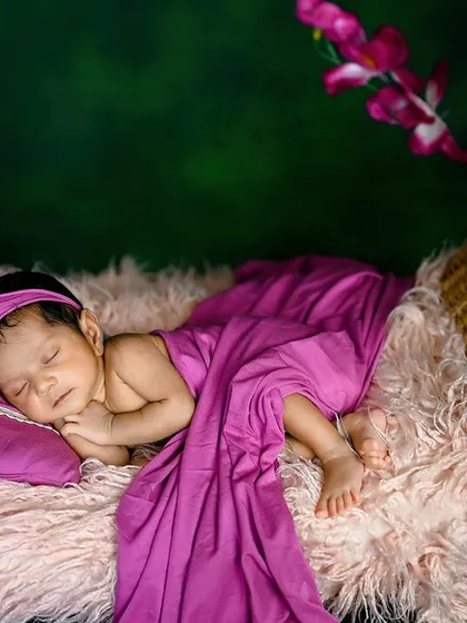 A beautiful composition of a newborn in a hanging basket, with a long purple drape and flowers.