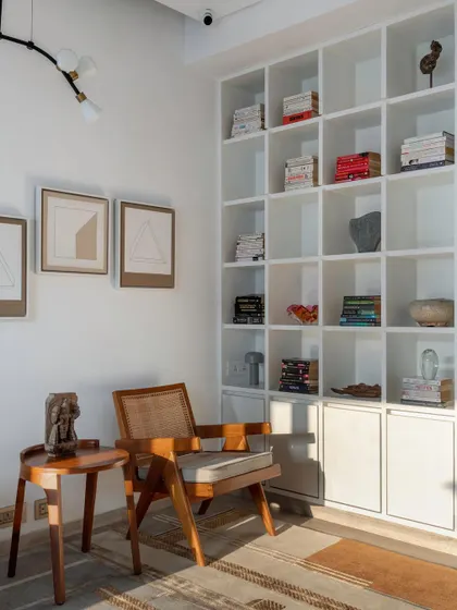 A library is infinity under a roof. This cozy reading corner features a large white bookshelf filled with books and art objects, paired with a classic wooden armchair, creating a perfect spot to get lost in a story.