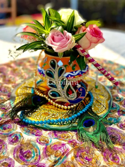 Another beautiful centerpiece detail, featuring a small pot decorated with a miniature peacock crown (mukut) and peacock feathers, surrounded by fresh roses.
