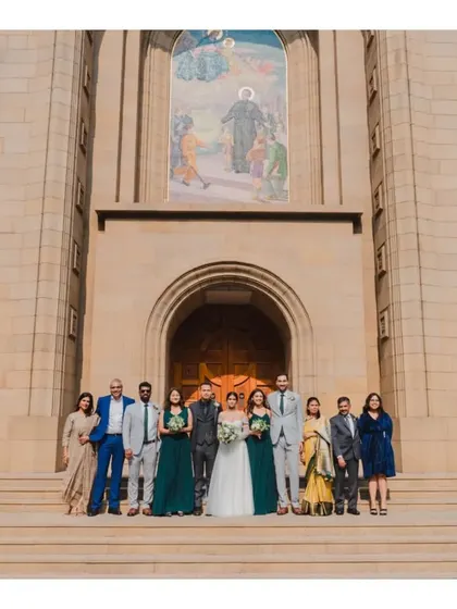 The wedding party posing on the steps of the grand church after the ceremony, a beautiful formal portrait of the couple with their closest friends and family.