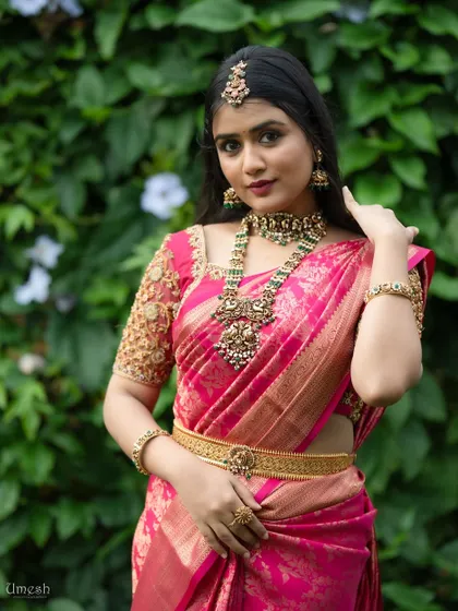 This look features a stunning antique choker and haram set against a vibrant pink saree. The intricate design and green stone accents make it a true statement piece.