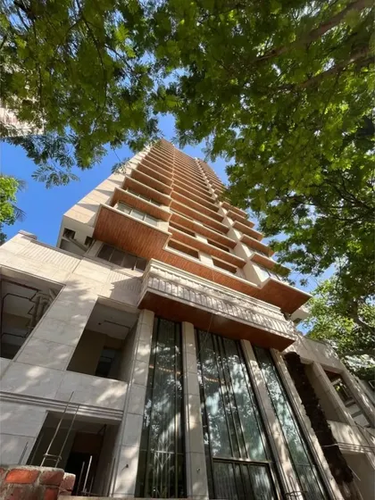 A view from the ground up of the tower under construction, framed by lush greenery. This shot captures the building's impressive scale and the integration of natural elements into the urban design.