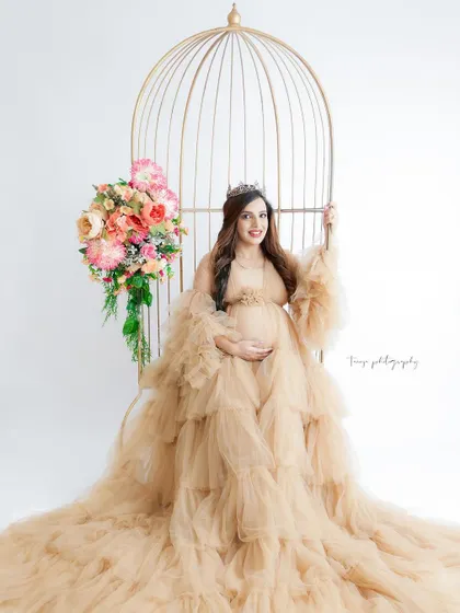 A glamorous portrait in a golden birdcage chair. The mom-to-be looks like a queen in her ruffled nude gown and tiara.