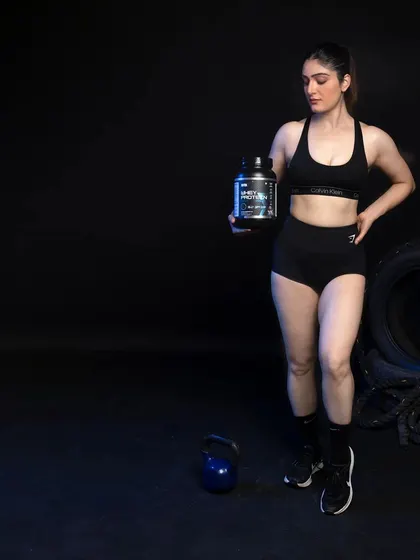 A female model standing with a kettlebell and a whey protein container, shot with dramatic lighting to create a powerful and moody image.
