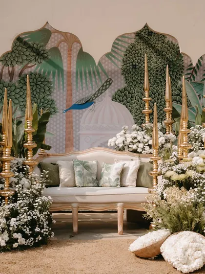 The full view of the personalized photo corner, with a comfortable sofa set against a stunning hand-painted mural depicting peacocks and palaces.