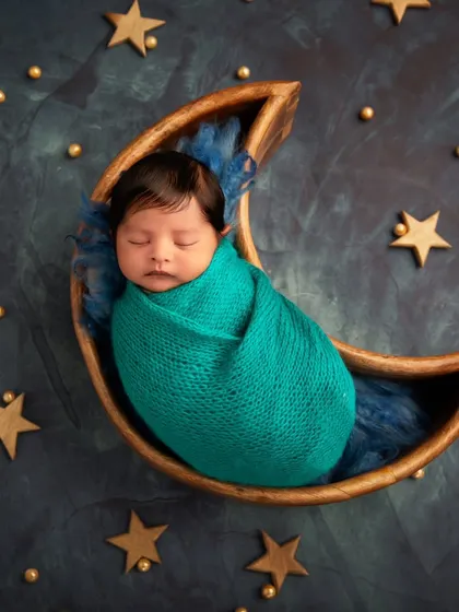 "Love you to the moon and back." This popular theme features a baby sleeping peacefully in a wooden moon prop, set against a starry night backdrop.