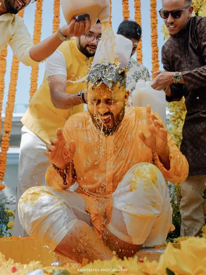 The groom gets a traditional milk bath during his Haldi, surrounded by friends and a backdrop of marigolds.