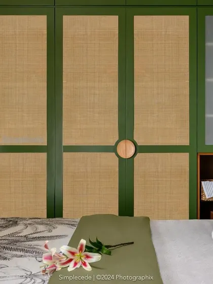 A close-up of the green and rattan wardrobe in the 'Cover me in Sunshine' master bedroom. The custom circular wooden handles are a unique detail that adds to the room's character.
