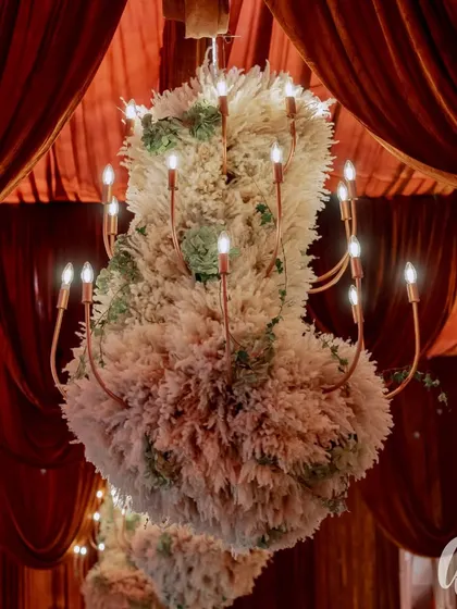 For this wedding, we designed custom chandeliers dressed in pampas grass and succulents, suspended from a ceiling of draped red velvet. This created a dramatic, textural contrast and a truly unique lighting feature.