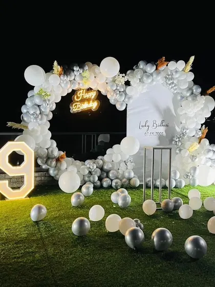 An elegant 19th birthday party on a lawn at night. The white and silver balloon arch and light-up numbers glow beautifully in the dark.