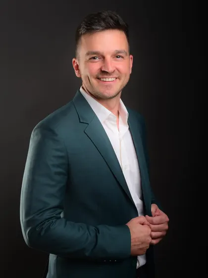 A welcoming and confident half-length portrait. The warm smile and open posture make the subject appear friendly and accessible.