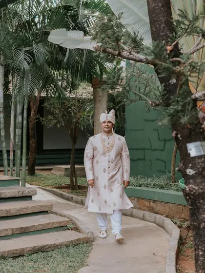 The groom, in his wedding sherwani, walks along a garden path, ready for the ceremony.