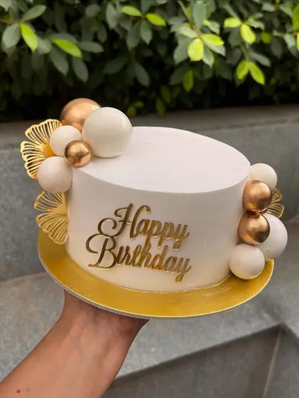 A simple and modern white and gold birthday cake. The design features a cluster of spheres and elegant gold fan toppers.