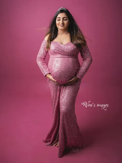 A queen in pink. Wearing a sparkling sequined gown and a tiara, this mother-to-be cradles her bump with a serene smile, looking every bit the royalty she is.