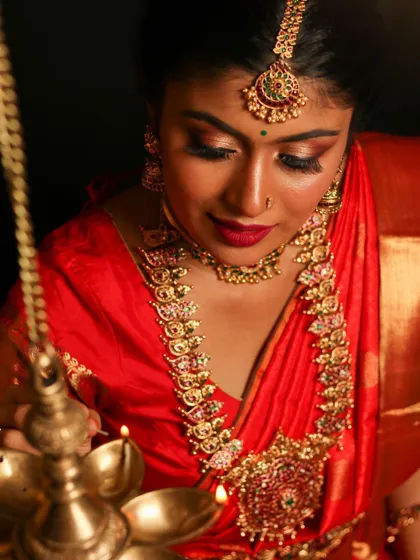 This Kemp jewelry set, with its vibrant red and green stones, is perfect for a classic bridal look. The set includes a choker, a longer haram with a large pendant, and a matching maang tikka, shown here by the warm light of a traditional lamp.