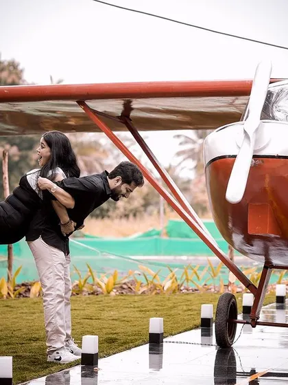A playful 'airplane' pose, with the groom lifting the bride in front of a small plane prop.