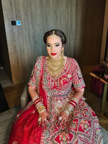 A regal bride in her magnificent red and gold lehenga. The makeup is bold and classic, with a strong red lip and defined eyes to match the grandeur of the occasion.