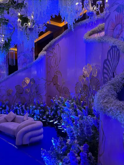 This reception stage features a unique, flowing design with floral accents against a softly lit, artistic backdrop. The curved lounge seating adds to the sophisticated and modern aesthetic.