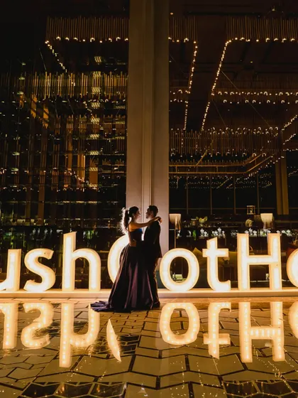 A couple poses in front of a large, illuminated sign with their wedding hashtag. This kind of personalized branding is a key element in our themed events.