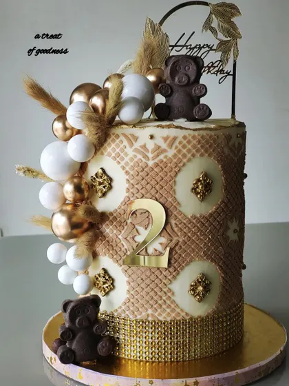 An elegant teddy bear-themed cake for a second birthday. I used a two-tone textured stencil and a cascade of white and gold spheres, finished with dried pampas grass for a bohemian touch.