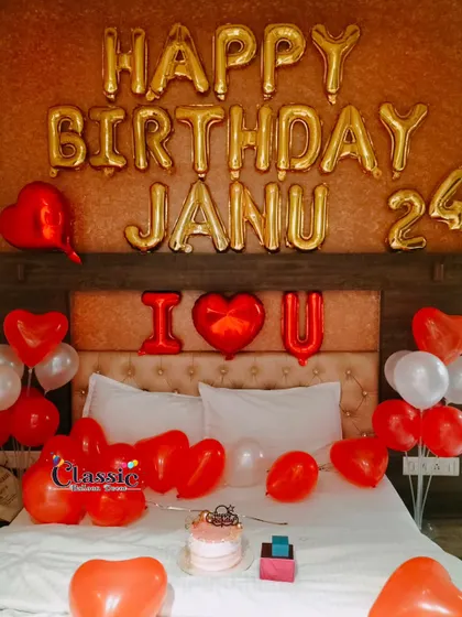 A romantic birthday bedroom decoration with red and white heart-shaped balloons, foil letters, and a cake ready for celebration.