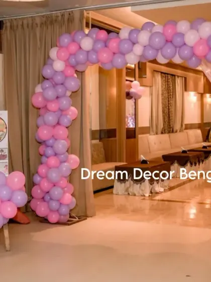 The entrance to Sakshi's butterfly-themed party, with a pink and purple balloon arch and a personalized milestone board.
