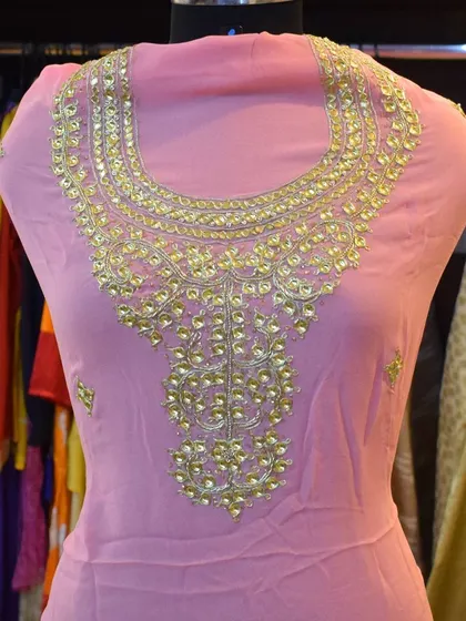 This pink suit features an elaborate, handcrafted neckline. This is an example of how we can customize a design based on a client's vision, turning a simple outfit into a statement piece.