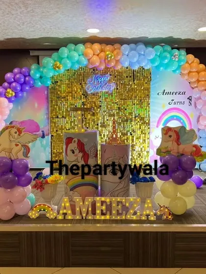 A large-scale unicorn theme setup on a stage, with a gold shimmer curtain and a rainbow of pastel balloons.