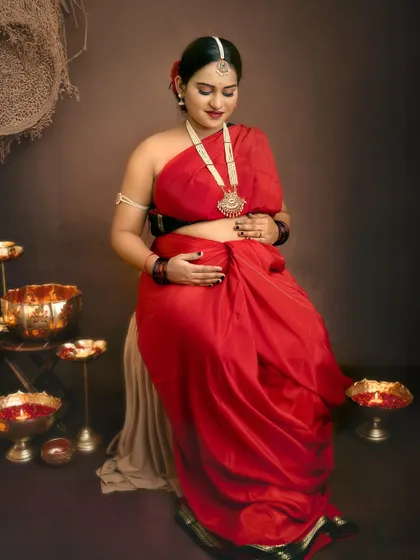 Seated amidst traditional brass lamps, this mother-to-be looks down at her bump with love, creating a peaceful and heartfelt image.