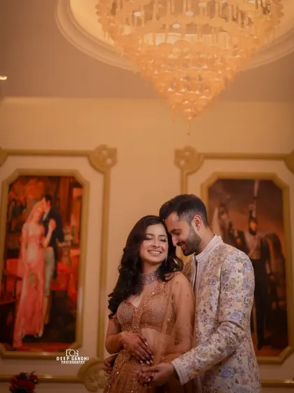 A happy, smiling portrait of the engaged couple. The warm, ambient light of the chandelier and the classic art in the background add to the elegant atmosphere.