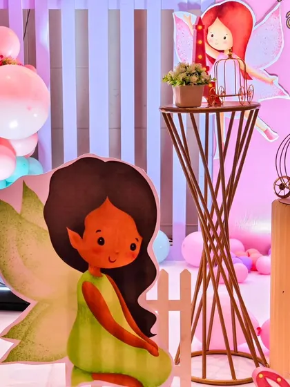 A cute fairy cutout stands next to a gold pedestal, part of the enchanted garden theme.