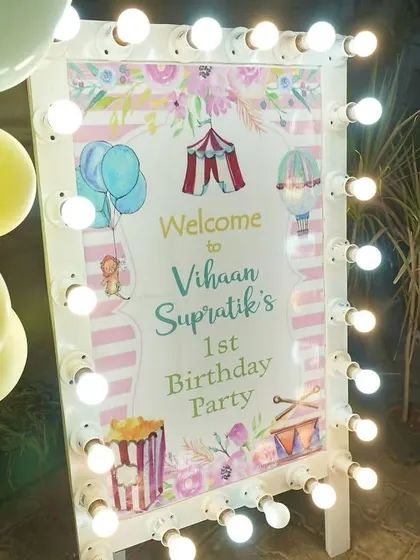 The welcome sign for Vihaan's first birthday party, featuring carnival-themed illustrations and a frame of classic marquee bulbs. It's all about creating an inviting atmosphere.