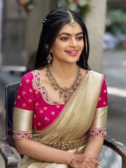 This bride's look for her event features a bright pink blouse and a cream saree. The makeup is soft and pretty, with a half-up hairstyle.